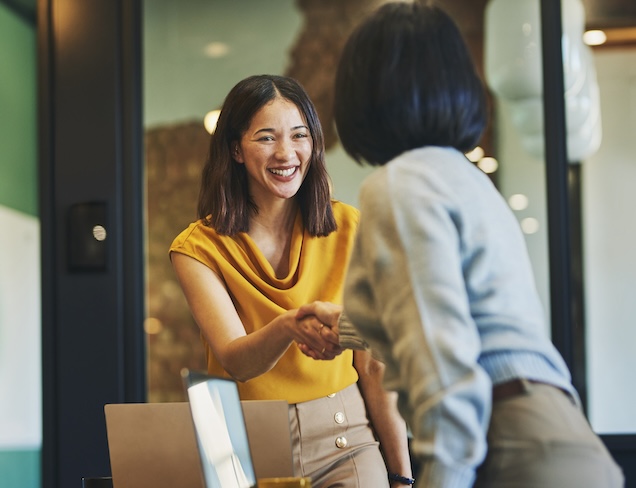 Businesswoman shaking hands with client and smiling cheerfully in meeting room